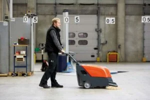 Ride-on scrubber dryer cleaning the floor of a large warehouse aisle